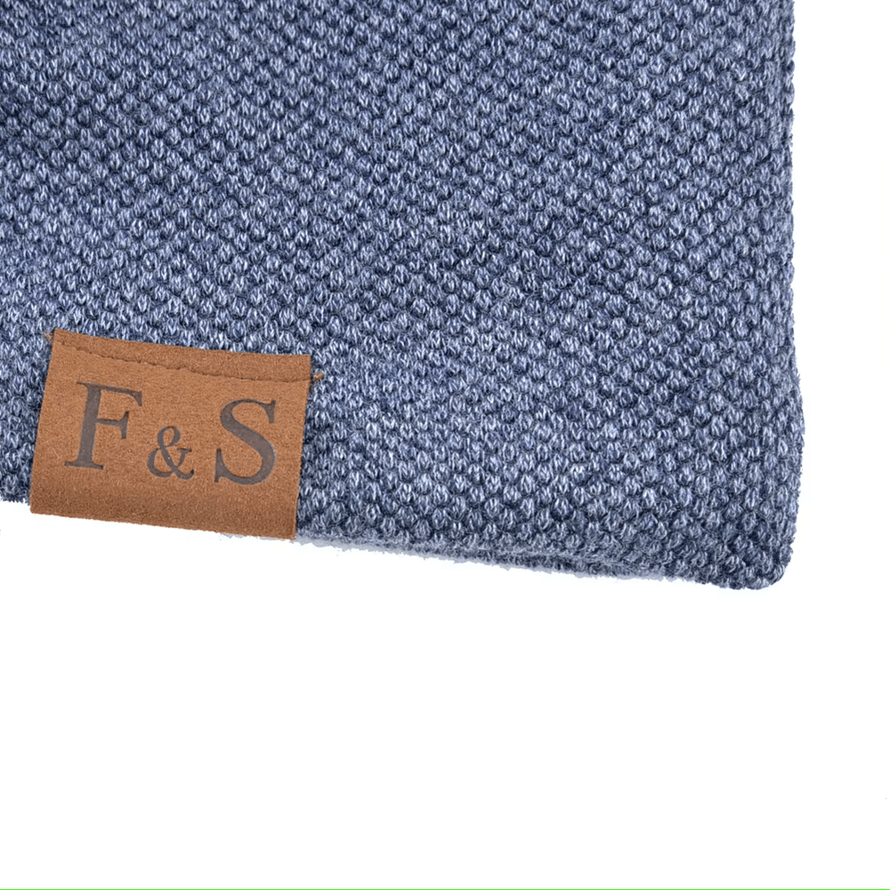 Close-up of a blue knit beanie with a stylish brown leather tag, featuring "F & S" text, perfect for casual wear.